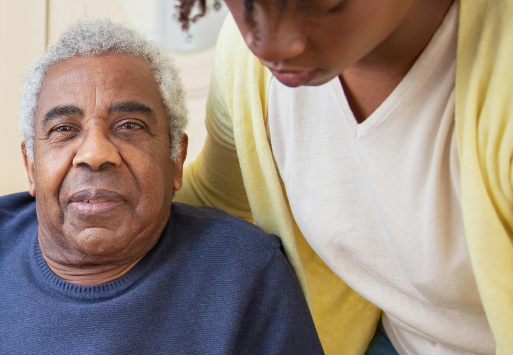 Close-up of an older African American man and a young African American woman. The man, seated, is looking directly at the camera with a calm, pleasant expression.