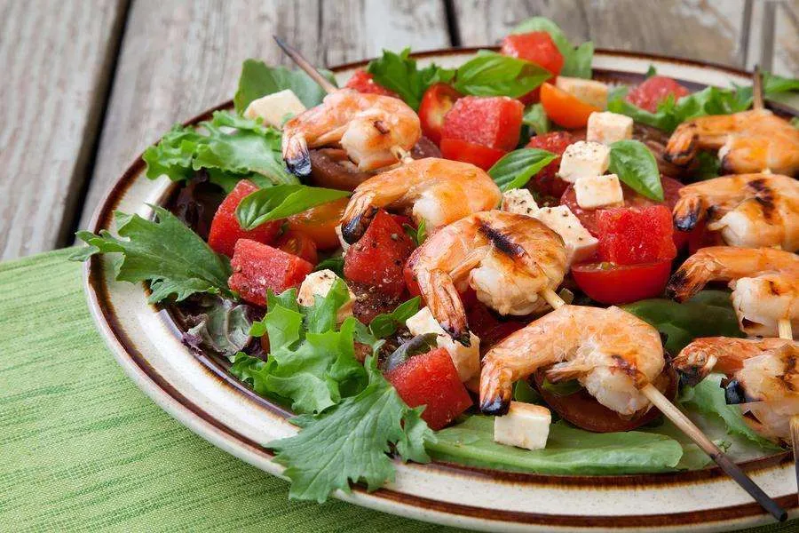 Close-up of a plate of shrimp skewers with a watermelon and feta salad.