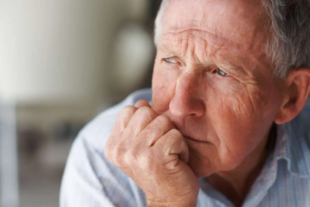 Close-up of a thoughtful older man. The man appears to be in his late 60s or 70s, with visible signs of aging on his face, including wrinkles and lines around the eyes, forehead, and mouth. His expression is pensive, with a focused, slightly downward gaze.