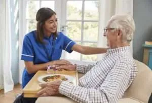 A medium shot of a young woman in a light-blue nurse's uniform assisting an elderly man.